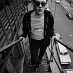 Black and white photograph of Andy Warhol in a Breton striped shirt and sunglasses ascending a fire escape above a city street