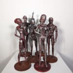 A group of six rust and silver-colored robot figurines, two with male anatomy and four with female anatomy, stand in varying positions on a white pedestal.