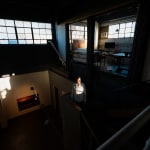 An artist, Curtis Mitchell, hit by a small patch of sunlight as he stands on a staircase in the center of a dark loft setting