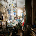 an artist, Vernita N'Cognita standing at the end of a hallway in a loft setting filled with plastic containers and other materials