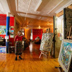 An artist, Claire Fergusson, stands amidst her many paintings in a light-filled loft setting