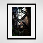 Framed photograph in black wood of an artist, Gerald Marks, standing beside potted plants in front of fire escape steps outside his loft art studio in Midtown
