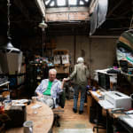 Two artists, Ken and Flo Jacobs in a loft setting filled with artworks, books, and tools