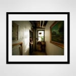 Black framed photograph of an artist and milliner, Christine Ellen, playfully peeks around a doorway of her loft space