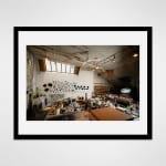 Framed photograph in black wood of a loft studio space filled with work desks and art materials and with walls adorned with black sculptures by artist Gilda Pervin