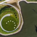 Public park with circular moon sculptures placed in a semicircle on a green lawn, next to a bay