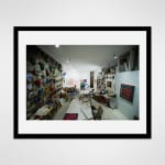 Framed photograph in black wood of two artists, Carolyn Oberst and Jeff Way, embracing in a loft space filled with work tables, an array of masks, and paintings
