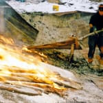 Photograph of a person shoveling with a large fire next to them.