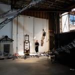 An artist, Marsha Pels, stands amongst sculptural works in a large industrial loft space