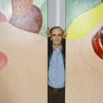 Photograph of Tom Wesselmann standing between two separated parts of a large painting of a female nude