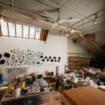 A loft studio space filled with work desks and art materials and with walls adorned with black sculptures by artist Gilda Pervin