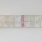A row of white iridescent cubes made of acrylic paint on MDF with a pale pink textured strip at its center is mounted on a white wall.