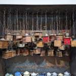 Detailed view of a steel box with an accumulation of wood coffee mills hanging from chains from its top interior and numerous enamel coffee pots at its base