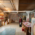 An artist, Steve Silver, standing at a work table amist numerous sculptures and paintings in an industrial loft setting