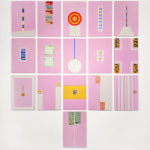 An array of colorful paintings comprised of geometric abstract forms displayed on a white wall