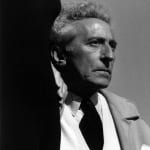 Black and white photograph of Jean Cocteau in a suit looking to the right with a dark shadow framing his left side