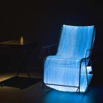 a chair made from optic fibers, sitting on a floor in a dark room and emitting a blue light