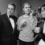 Black and white photograph of three people, Andy Warhol, Marisol, and a man, holding cups at a party