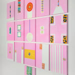 An array of colorful paintings comprised of geometric abstract forms displayed on a white wall