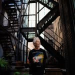 An artist, Gerald Marks, standing beside potted plants in front of fire escape steps outside his loft art studio in Midtown
