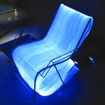 View angled from above of a chair made from optic fibers, sitting on a floor in a dark room and emitting a blue light