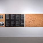 Installation view of two photographs and eight pages of white text on black paper next to a map drawing on plywood