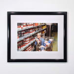 Framed Photograph of Andy Warhol crouching in a grocery store aisle, selecting cans of soup behind a shopping cart