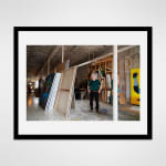 Framed photograph in black wood of an artist, Carmen Cicero, standing amidst large-scale paintings in an industrial loft setting