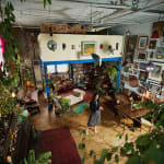 An artist, Jennifer Charles, standing in the center of her loft studio adorned richly adorned with pictures and plants
