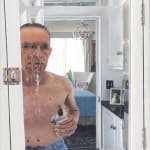 This image is a hyper-realistic painting that captures a shirtless man standing in front of a bathroom medicine cabinet mirror, which is slightly ajar. The man is using a nasal spray, and the action is captured mid-spray, with a stream of the liquid visib