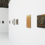 side angle view of wall with 6 small paintings hung horizontally next to perpendicular wall with four small paintings also hung horizontally