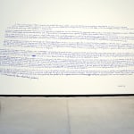Installation consisting of two wooden trestles, placed in front of a wall with inscriptions.