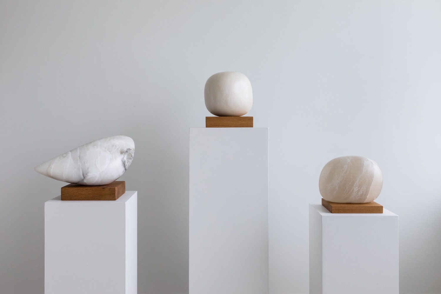 Three alabaster Aya Miyatake sculptures on plinths at varied heights, the center plinth the tallest of the group.
