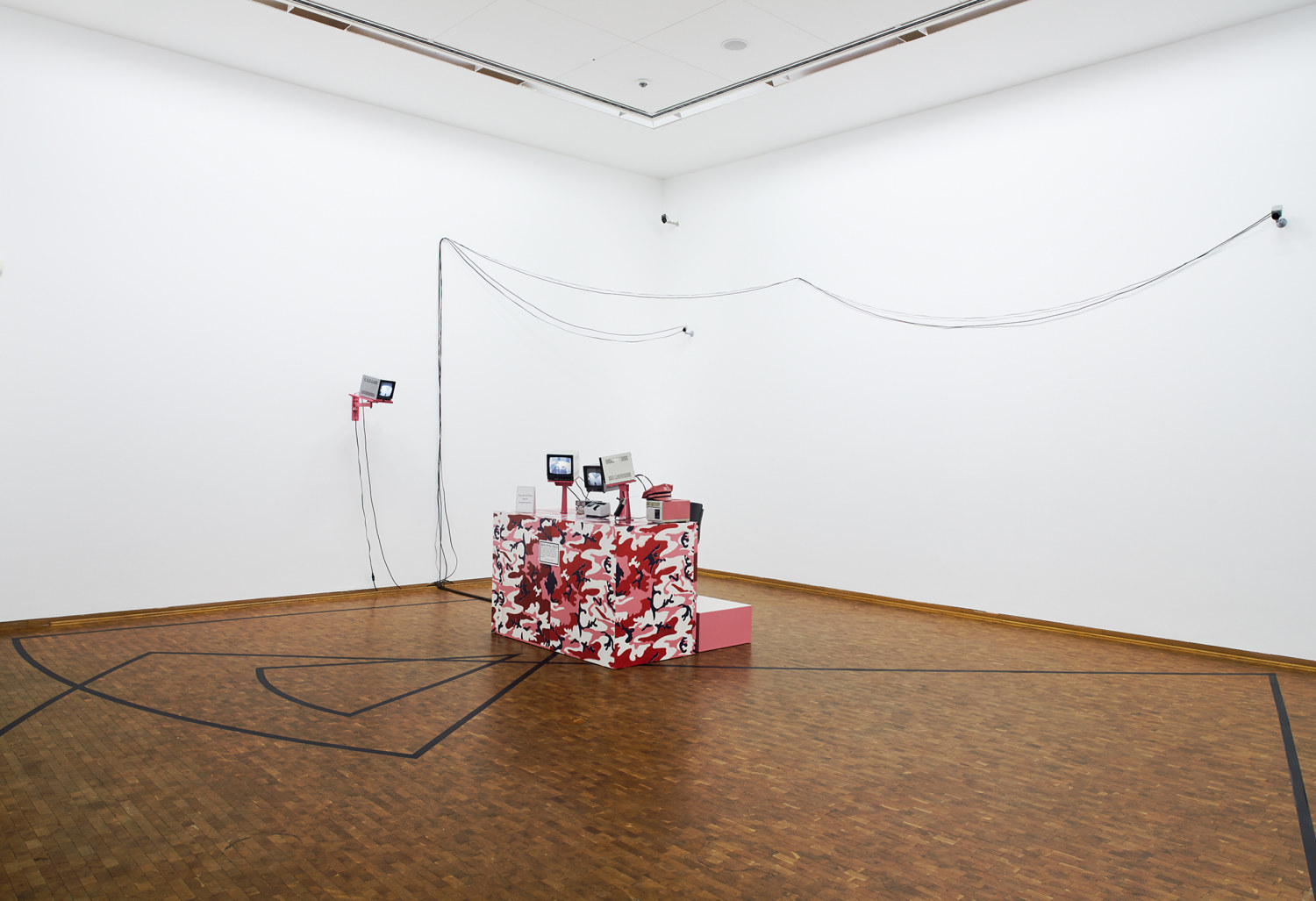 Julia Scher, Security By Julia X, 1991, camouflage-painted desk, wooden platform, chair, monitors, video printer, printing paper rolls, signage, switchers,...