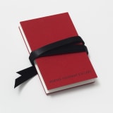 Small red book inscribed with the words "Marian Goodman Gallery" wrapped with a black ribbon.