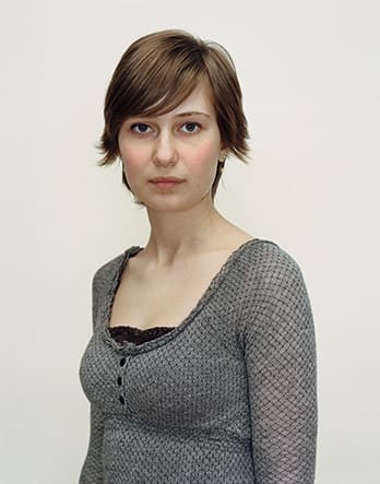 A Rineke Dijkstra portrait of a woman in a gray shirt with short hair.