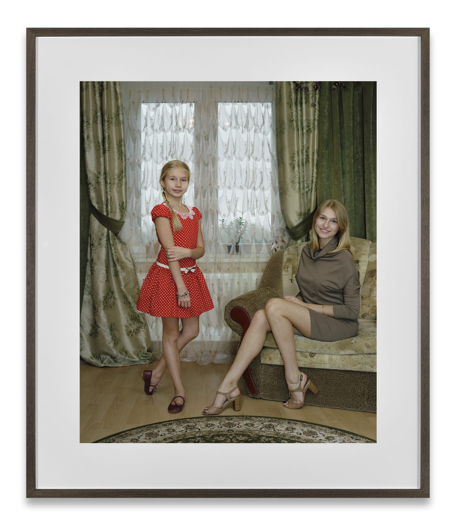 A framed photograph by Rineke Dijkstra of a girl in a red dress and a woman in a beige dress in an elegant living room.