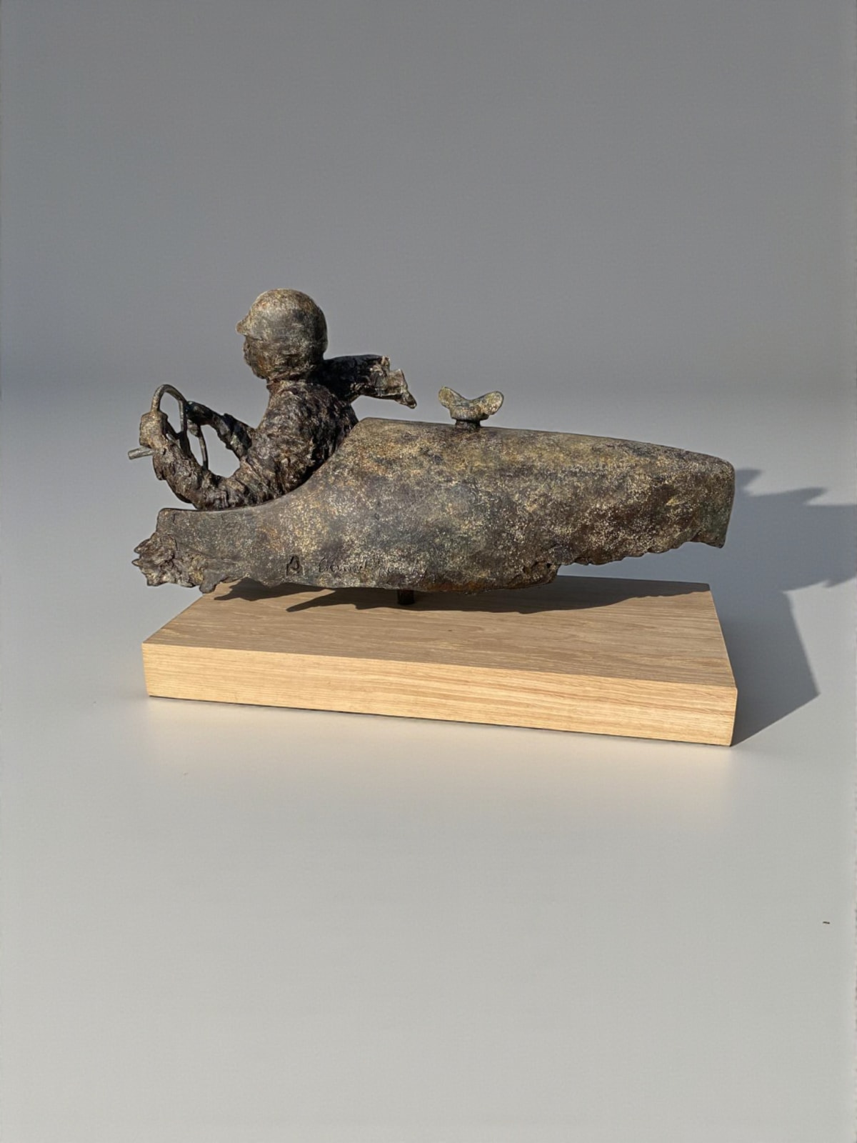 Sculpture en bronze “Master of Speed V” de Lieven D’Haese, représentant un personnage assis dans un véhicule stylisé avec un petit oiseau posé à l’avant.