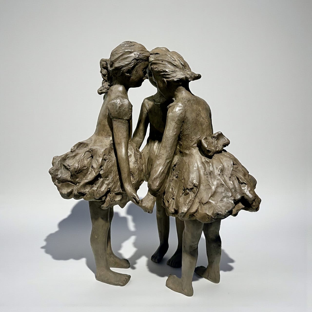 scultura in bronzo, Le Tre Grazie, Béatrice Cols, artista belga, bambini in bronzo, scultura figurativa, bambine in cerchio, abiti svolazzanti, arte contemporanea, scultura poetica, decorazione interni, scultura da giardino, bronzo patinato, opera da collezione, scultura decorativa