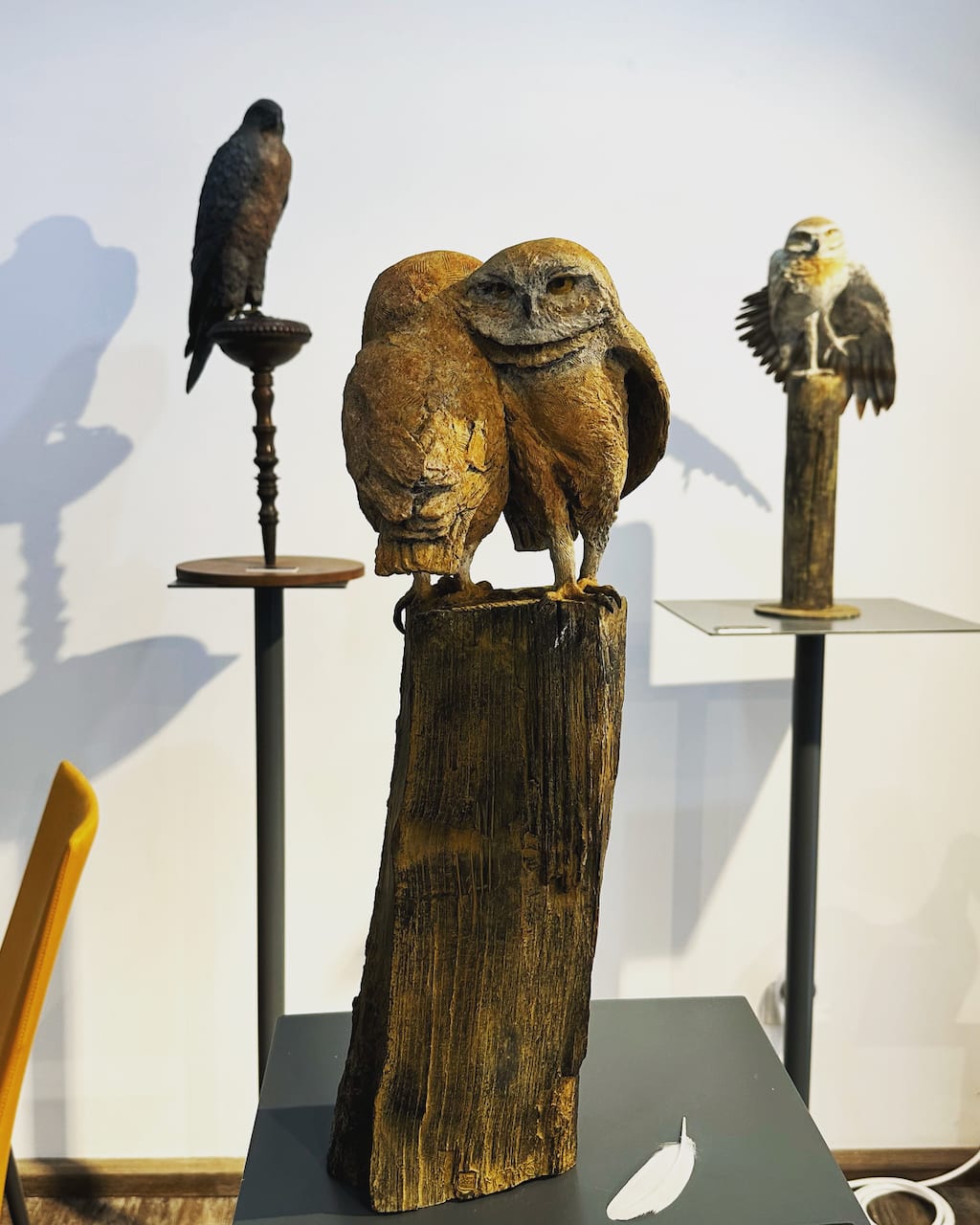 bronzen beeld, stel steenuilen in omhelzing, Marie Thys Belgische dierenkunstenares, bronzen uilen op houten stam, okerkleurige patina, romantisch dierbeeld, dierlijke verbondenheid, hedendaagse kunst, tuinbeeld, verzamelbronzen sculptuur, buitenbevestiging, Art Thema Gallery