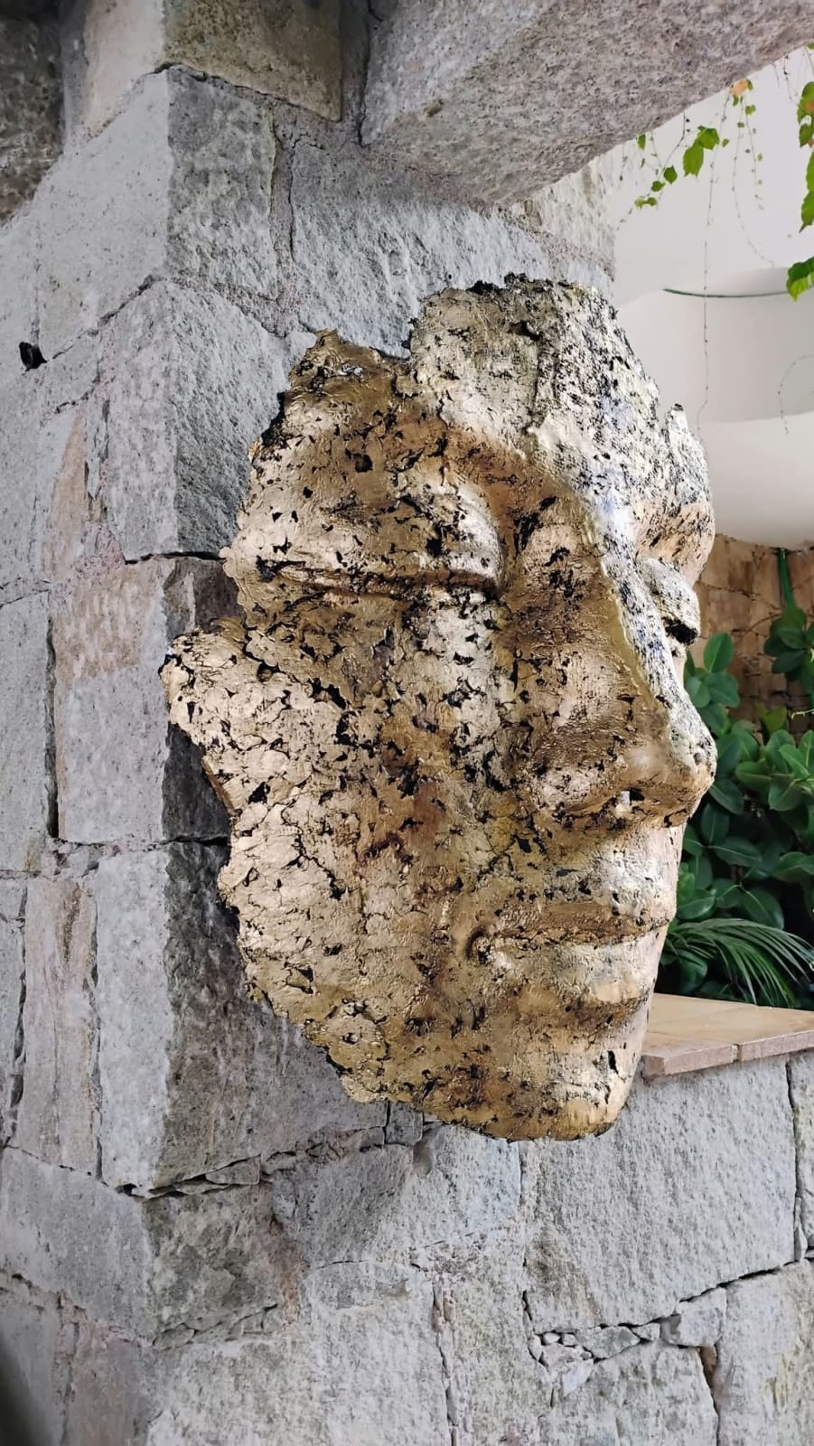 Sculpture murale contemporaine représentant un masque, en alliage avec feuille d’or et patine noire, œuvre expressive pour architecture intérieure.