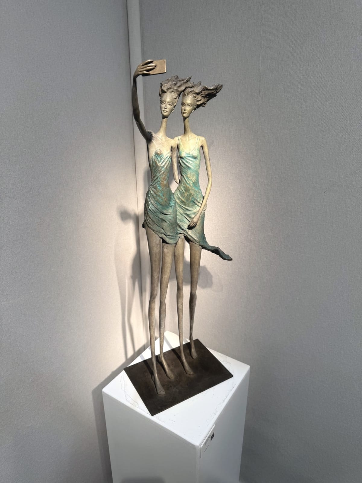 Deux Amies pour toujours deux filles sculpture de Hedwige Leroux sculpture contemporaine en bronze danseuse femme sculpture deux filles sœurs dans une robe verte et bleue prenant un selfie avec un téléphone ensemble à la galerie Art Yi à Bruxelles