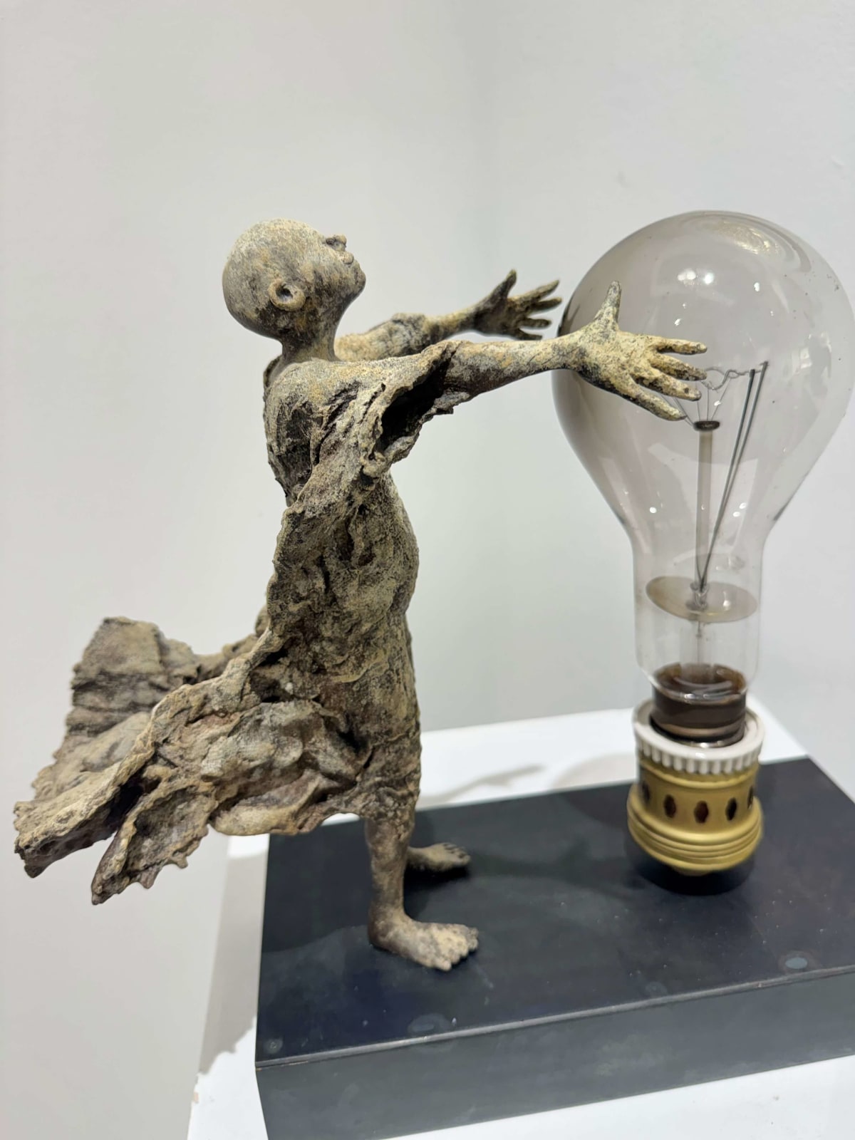 Visionary XL, sculpture lumineuse en bronze de Lieven d'Haese représentant un garçon ouvrant les bras pour allumer une ampoule, symbole d'imagination, de magie et de rêve. Sculpture d'art contemporain, design lumineux et design d'intérieur, exposée à la galerie Art Yi à Bruxelles.