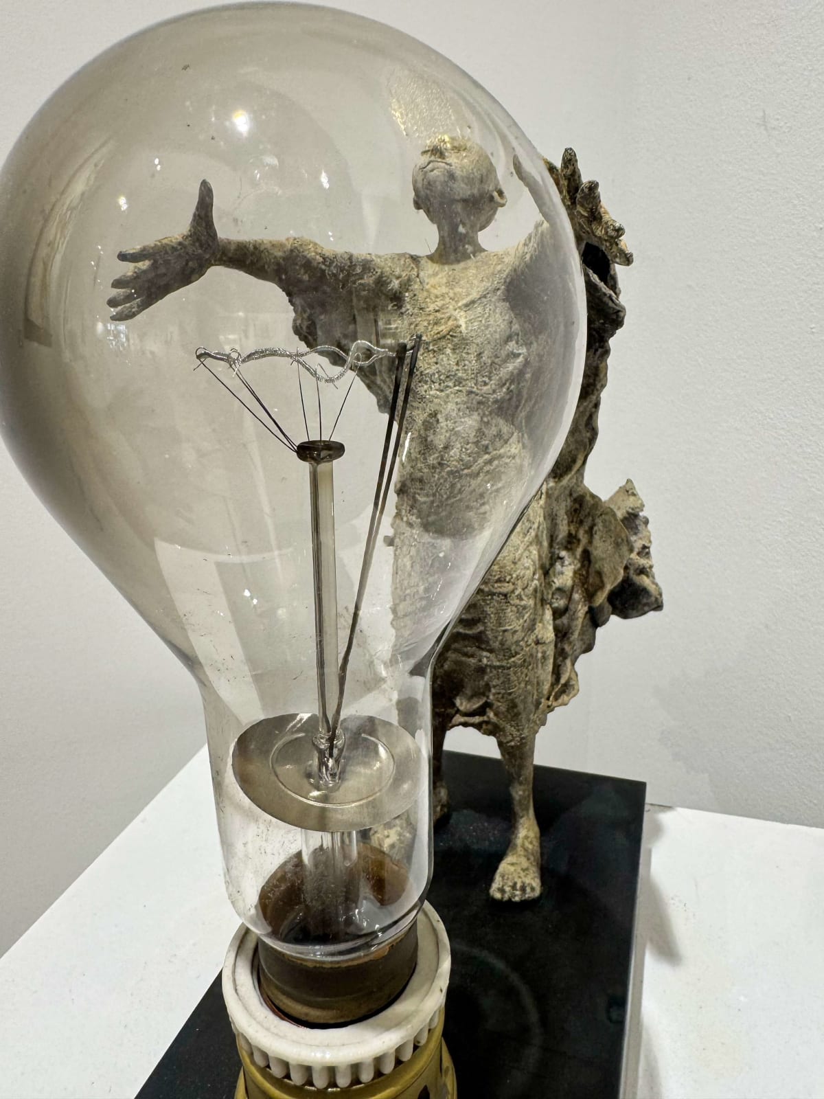 Visionary XL, sculpture lumineuse en bronze de Lieven d'Haese représentant un garçon ouvrant les bras pour allumer une ampoule, symbole d'imagination, de magie et de rêve. Sculpture d'art contemporain, design lumineux et design d'intérieur, exposée à la galerie Art Yi à Bruxelles.