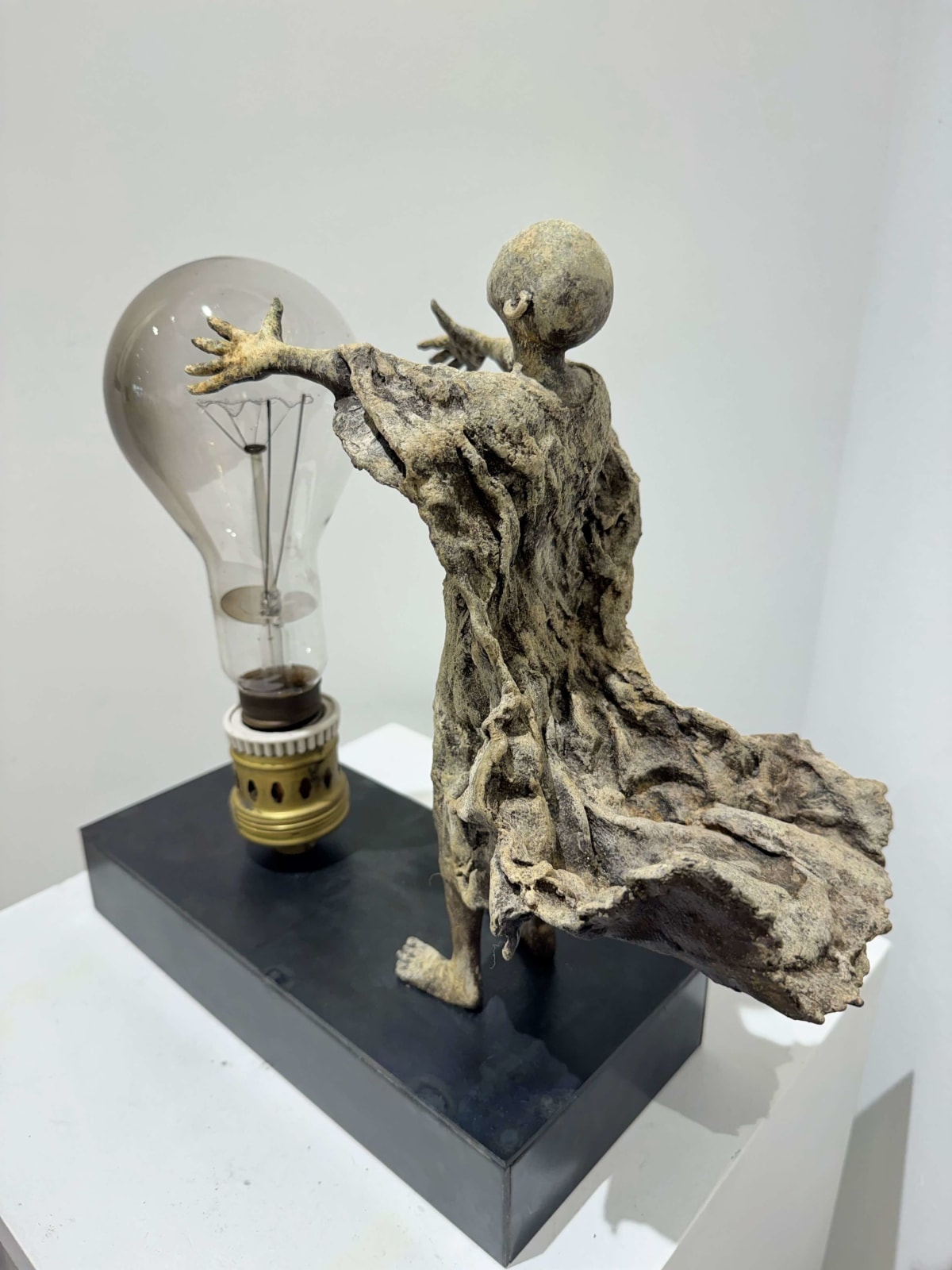 Visionary XL met lichtgevende jongen sculptuur, bronzen sculptuur van Lieven d'Haese, tuinsculptuur van een jongen die zijn armen opent om een ​​gloeilamp in zijn handen aan te steken met verbeeldingskracht, magie, droom, hedendaagse kunstsculptuur, licht, interieurontwerp in de Art Yi galerie in Brussel.