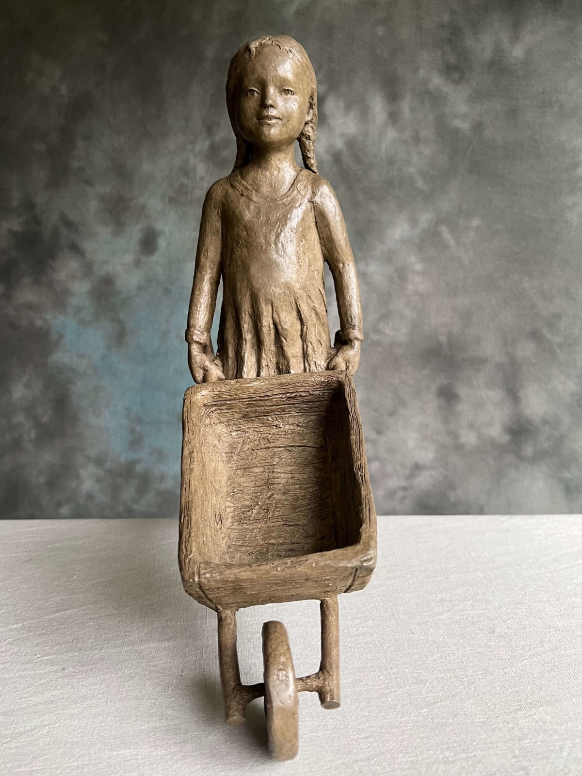 Het kruiwagenbeeld Sylvie Debray Gaudissart dierensculptuur hedendaagse bronzen kindersculptuur een schattig meisje dat een kar duwt kleine sculptuur tuindecoratie kunstgalerie Brussel België yi-kunst