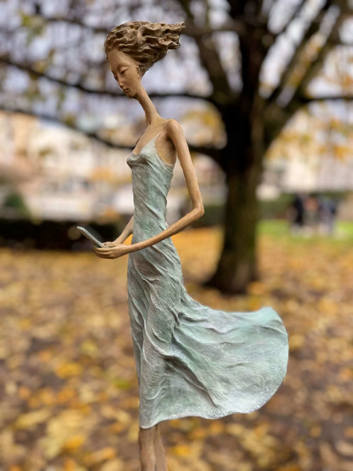 En attendant un signe sculpture d'Hedwige Leroux une sculpture de fille sculpture contemporaine sculpture de femme contemporaine sculpture en bronze une jeune fille marchant dans sa robe verte et tapotant sur le téléphone pour attendre un message Galerie Art Yi Galerie d'art de Bruxelles