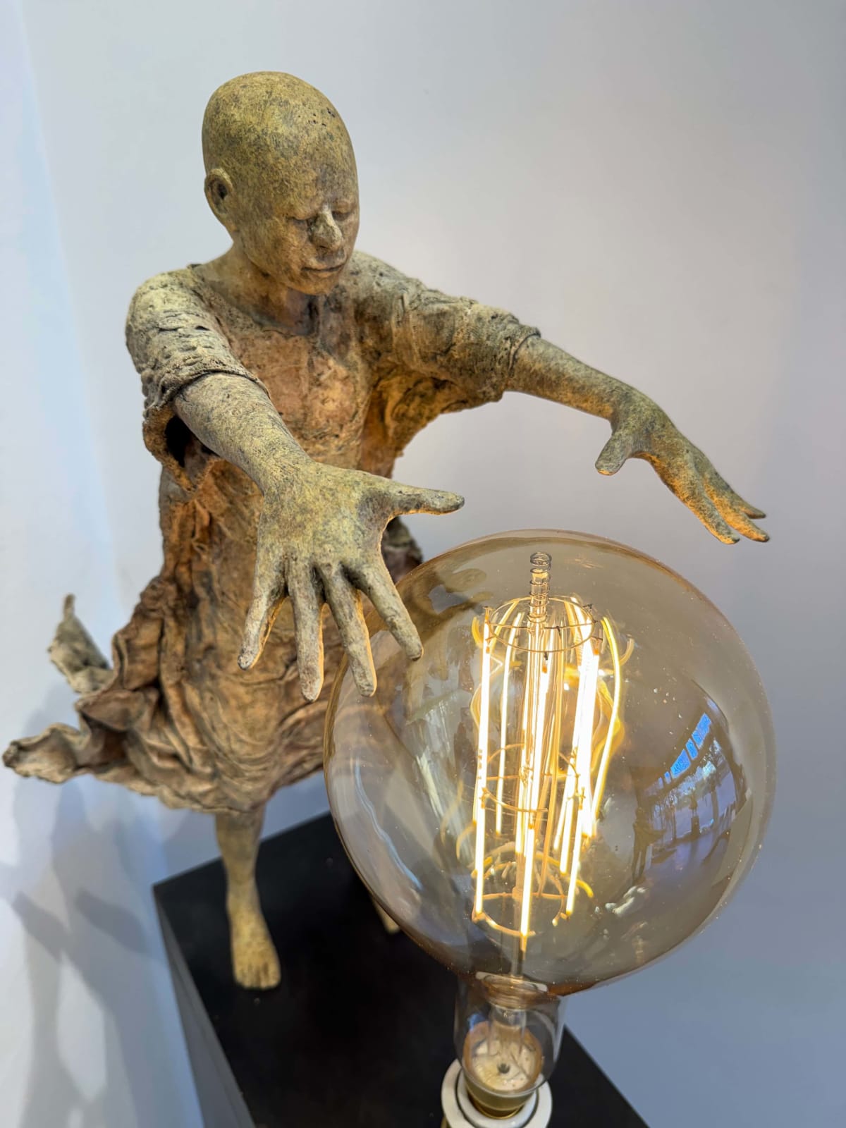 Visionary XL, sculpture lumineuse en bronze de Lieven d'Haese représentant un garçon ouvrant les bras pour allumer une ampoule, symbole d'imagination, de magie et de rêve. Sculpture d'art contemporain, design lumineux et design d'intérieur, exposée à la galerie Art Yi à Bruxelles.