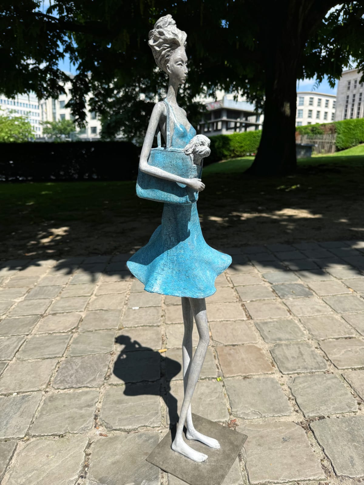Fifth Avenue, zeitgenössische Frauenskulptur Hedwige Leroux, ein junges Mädchen in einem blauen Kleid, das im Wind weht, während sie einen kleinen Hund in ihrer Tasche trägt, Bronzeskulptur Art Yi-Galerie Brüsseler Kunstgalerie