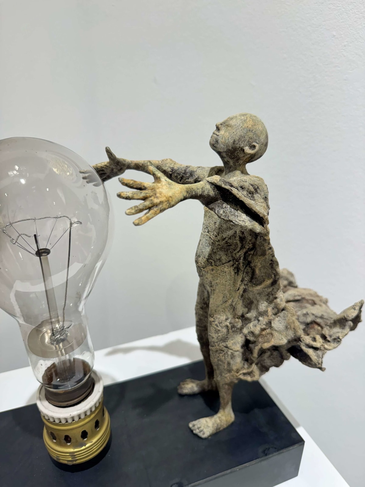 Visionary XL met lichtgevende jongen sculptuur, bronzen sculptuur van Lieven d'Haese, tuinsculptuur van een jongen die zijn armen opent om een ​​gloeilamp in zijn handen aan te steken met verbeeldingskracht, magie, droom, hedendaagse kunstsculptuur, licht, interieurontwerp in de Art Yi galerie in Brussel.